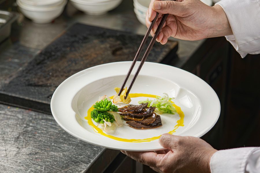 厨师在灶台前为菜品装盘,只见手部与厨师服